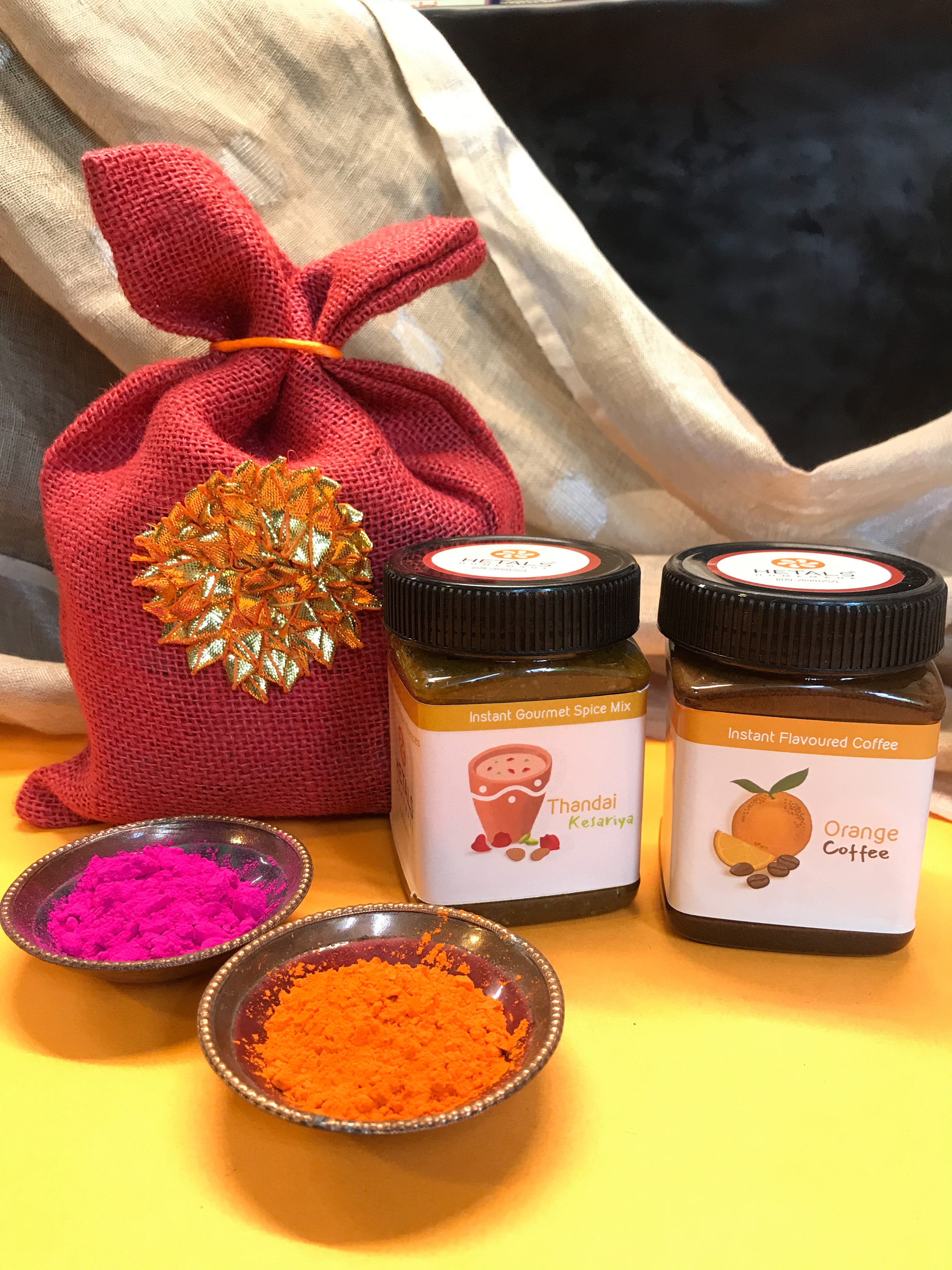 An image of Hetal's Homemade Holi Hamper. The hamper consists of two of our products, Thandai and Orange flavoured instant coffee. The image also shows the packaging of the hamper.
